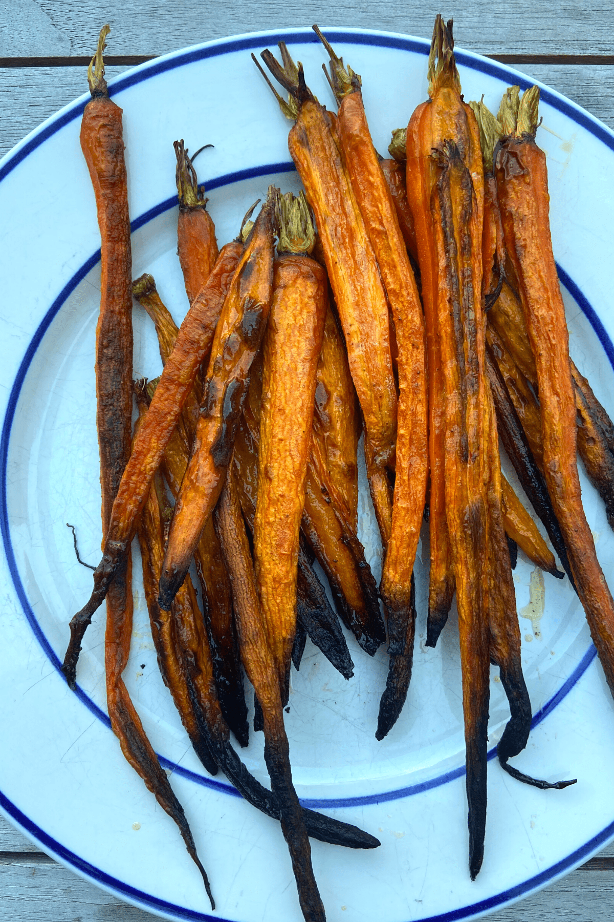 crispy roasted carrots piled on a white plate with blue rim