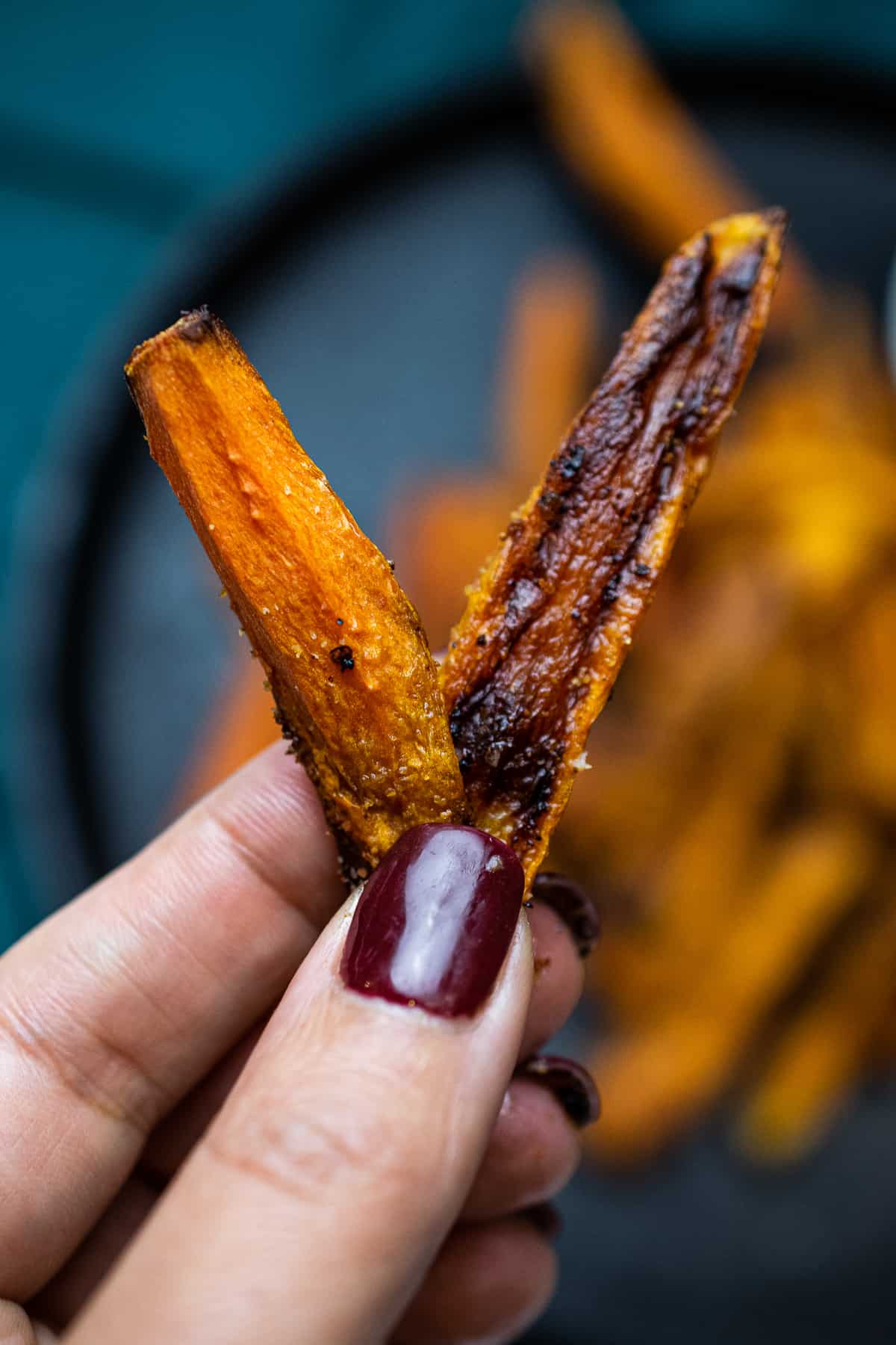 two carrot fries held by hand with painted nails