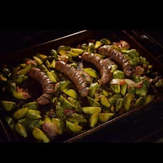 brussel sprouts and bratwurt with bacon on a sheet pan roasting in the oven