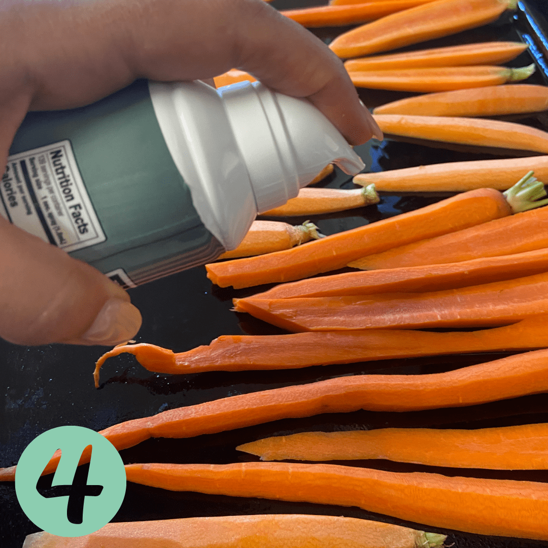 spraying carrots on a sheet pan with olive oil for roasting