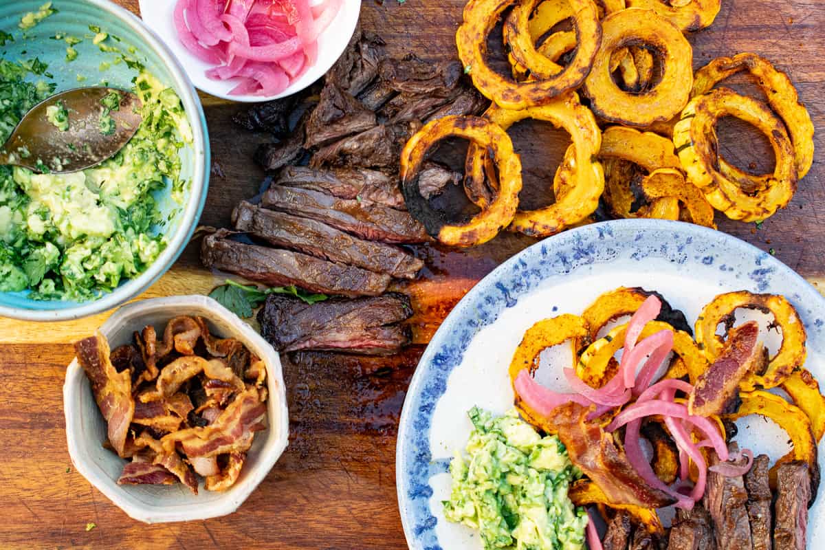 shot of delicata squash steak nachos 
-slicked steak on cutting board with crispy rounds of delicata squash, a bowl with guac, a small bowl with bacon and a plate with the dish served