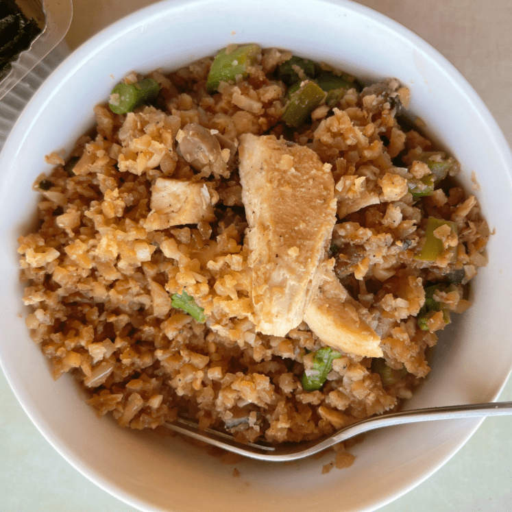 close up of a white bowl with keto chicken and rice skillet inside, chunks of chicken on top and a fork to the left