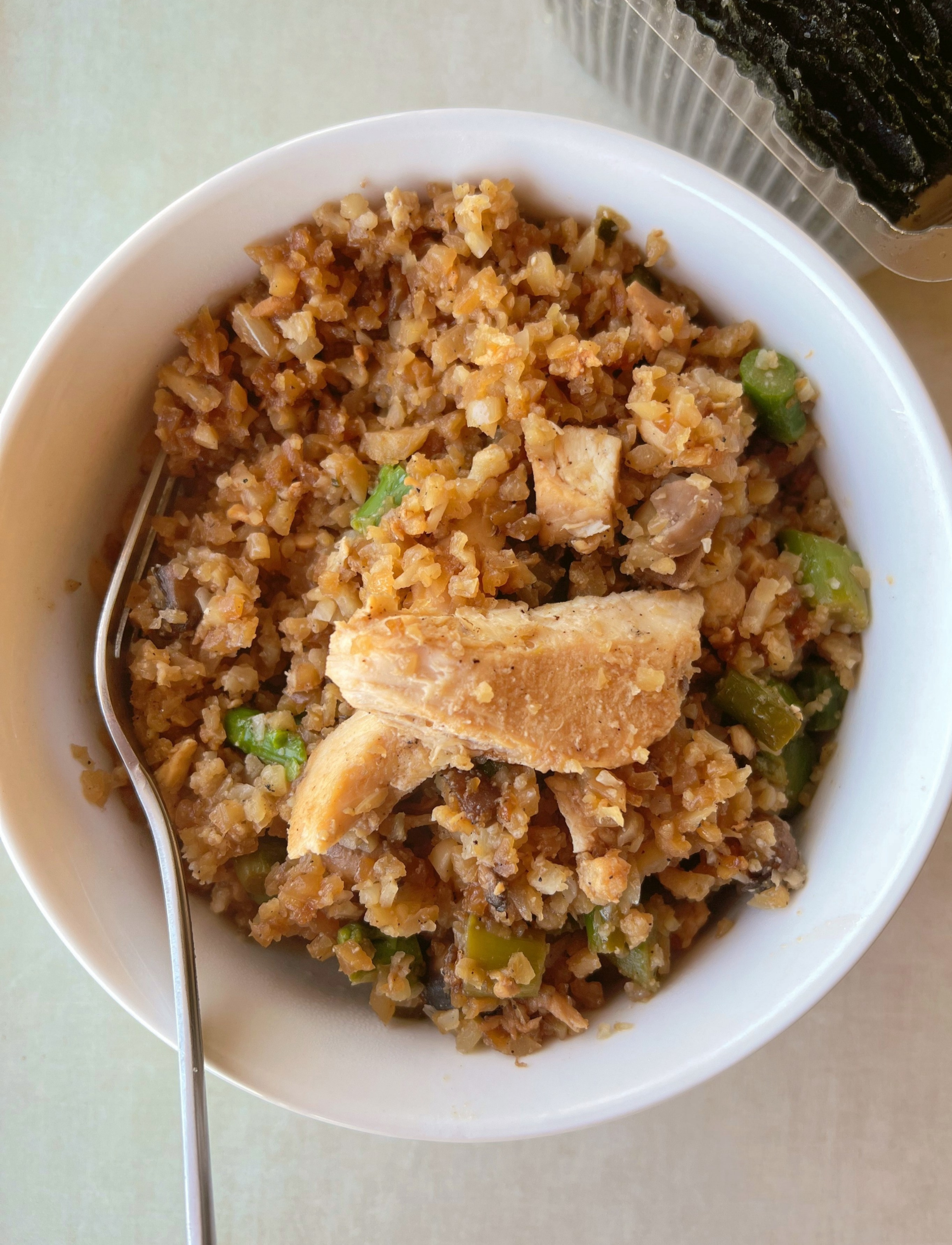 close up of a white bowl with whole30 chicken and rice skillet inside, chunks of chicken on top and a fork to the left