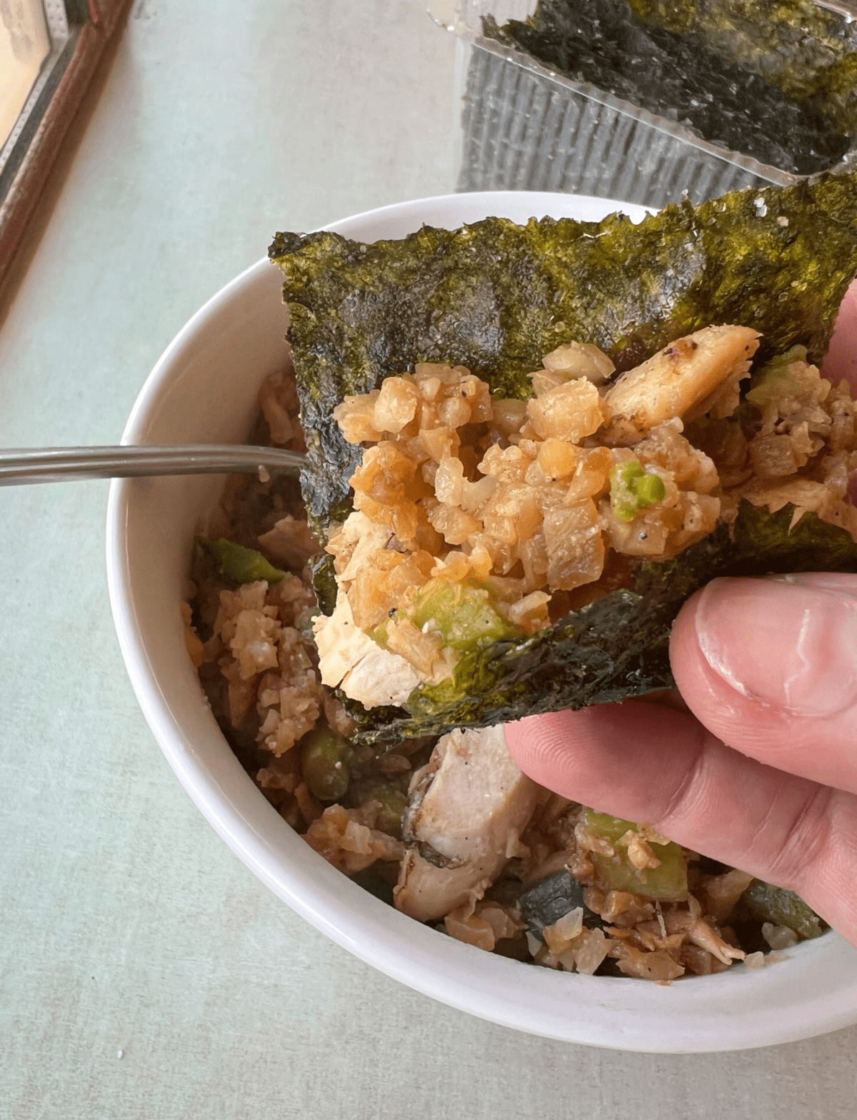 hand holing a small sheet of nori stuffed with whole30 chicken and rice mix over a bowl