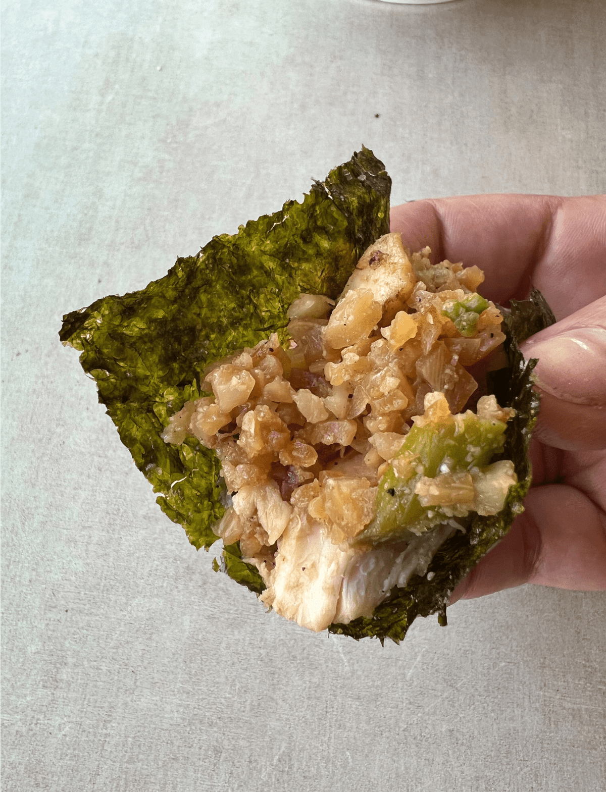 hand holing a small sheet of nori stuffed with whole30 chicken and rice mix