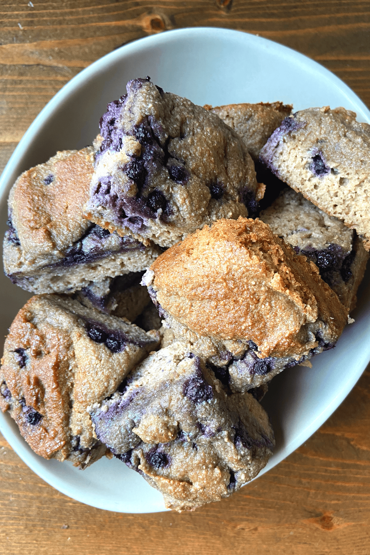 a brown table with a shallow grey bowl, full of nut free blueberry muffins