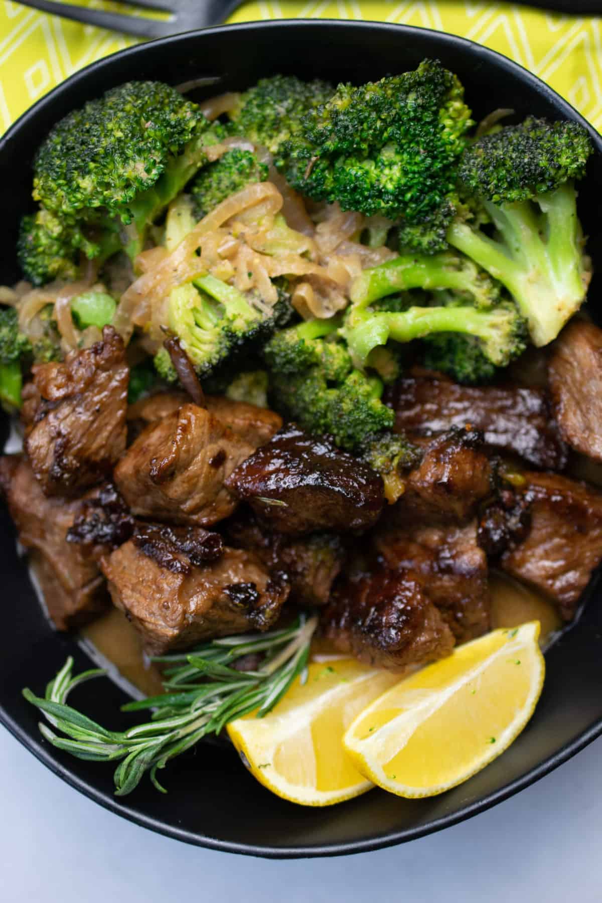 AIP lemon herb beef and broccoli close up. garnished with onion, rosemary sprig, and lemon wedges