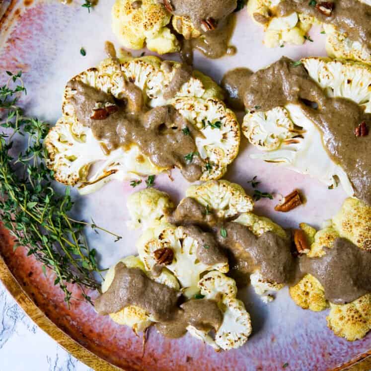 cauliflower steaks on a flatter with a thick drizzle of brown sauce and pecan pieces