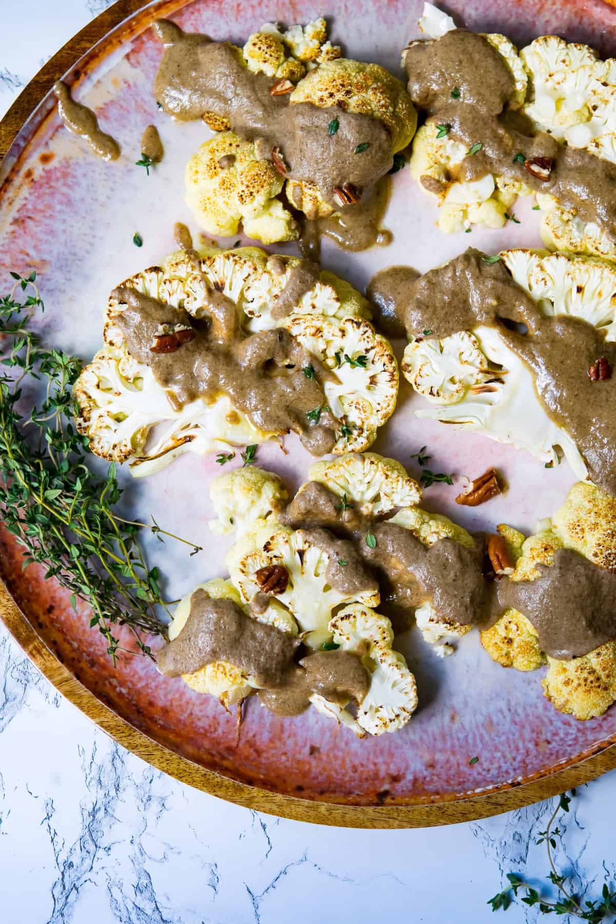 cauliflower steaks on a flatter with a thick drizzle of brown sauce and pecan pieces