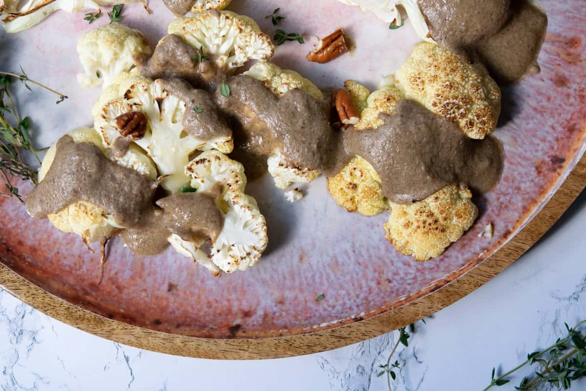 cauliflower steaks on a flatter with a thick drizzle of brown sauce and pecan pieces