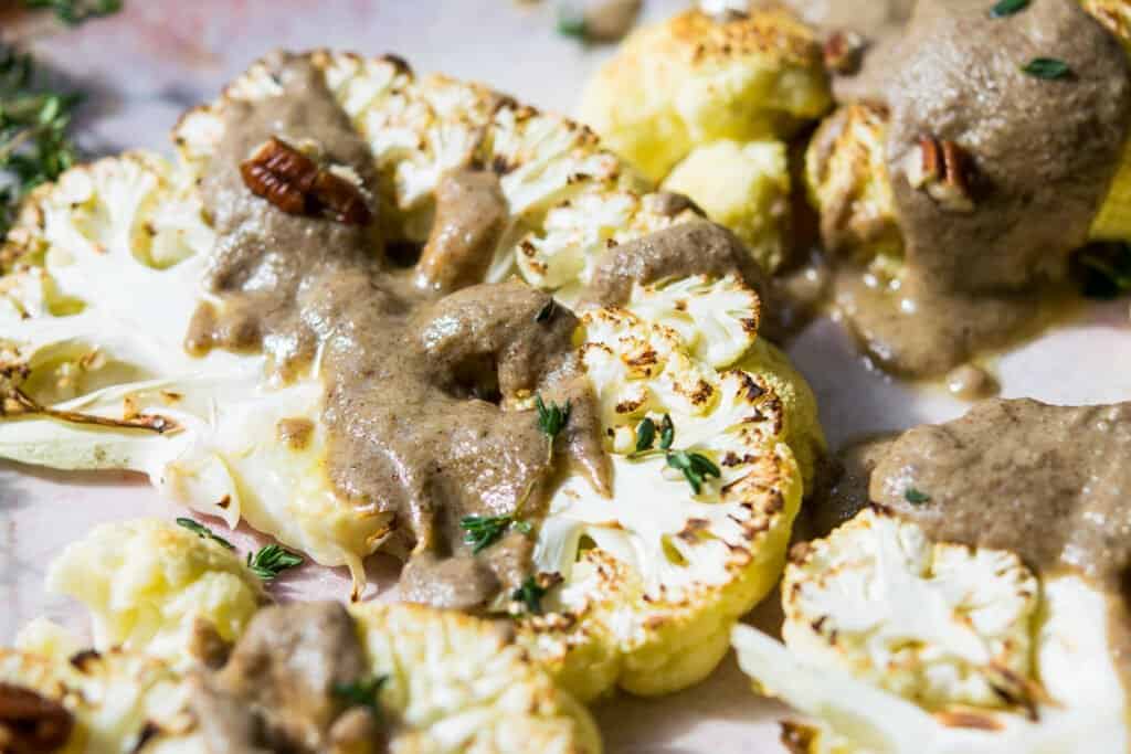 close up ofcauliflower steaks on a flatter with a thick drizzle of brown sauce and pecan pieces