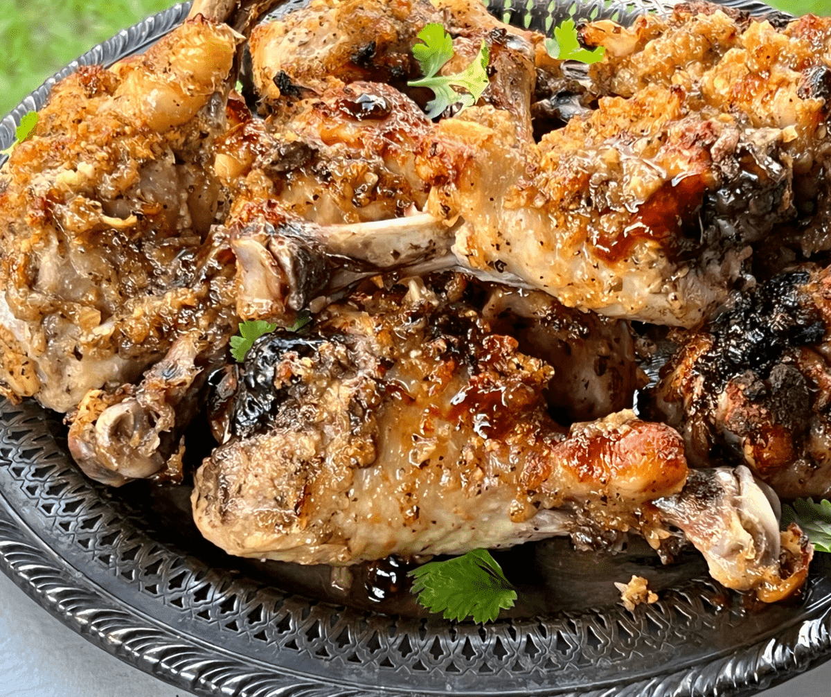 a pile of paleo huli huli chicken drumsticks on a silver platter with cilantro leaves on top