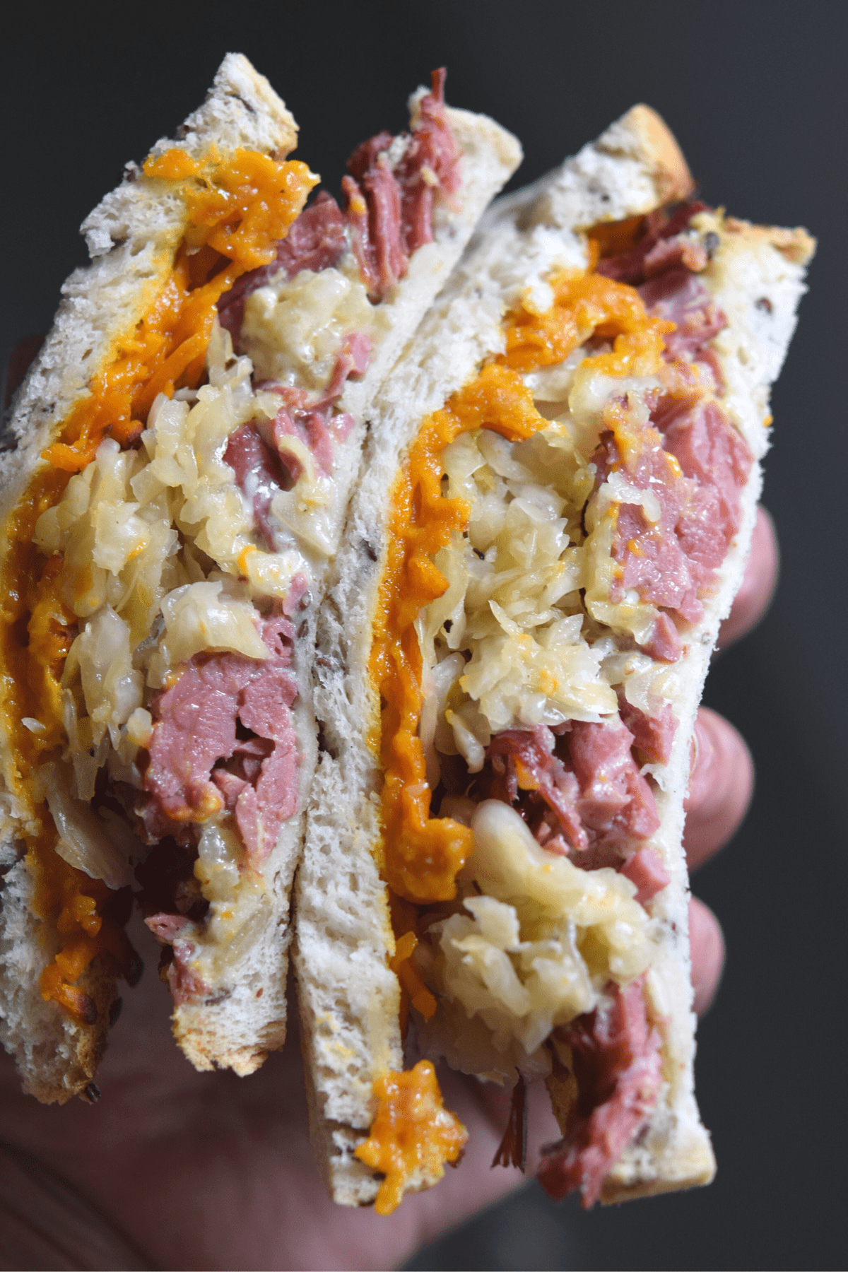 keto reuben sandwich stacked and held in hand, you see the melted cheese, sauerkraut and meat on toasted bread