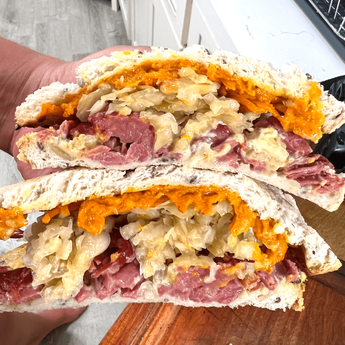 keto reuben sandwich stacked and held in hand, you see the melted cheese, sauerkraut and meat on toasted bread