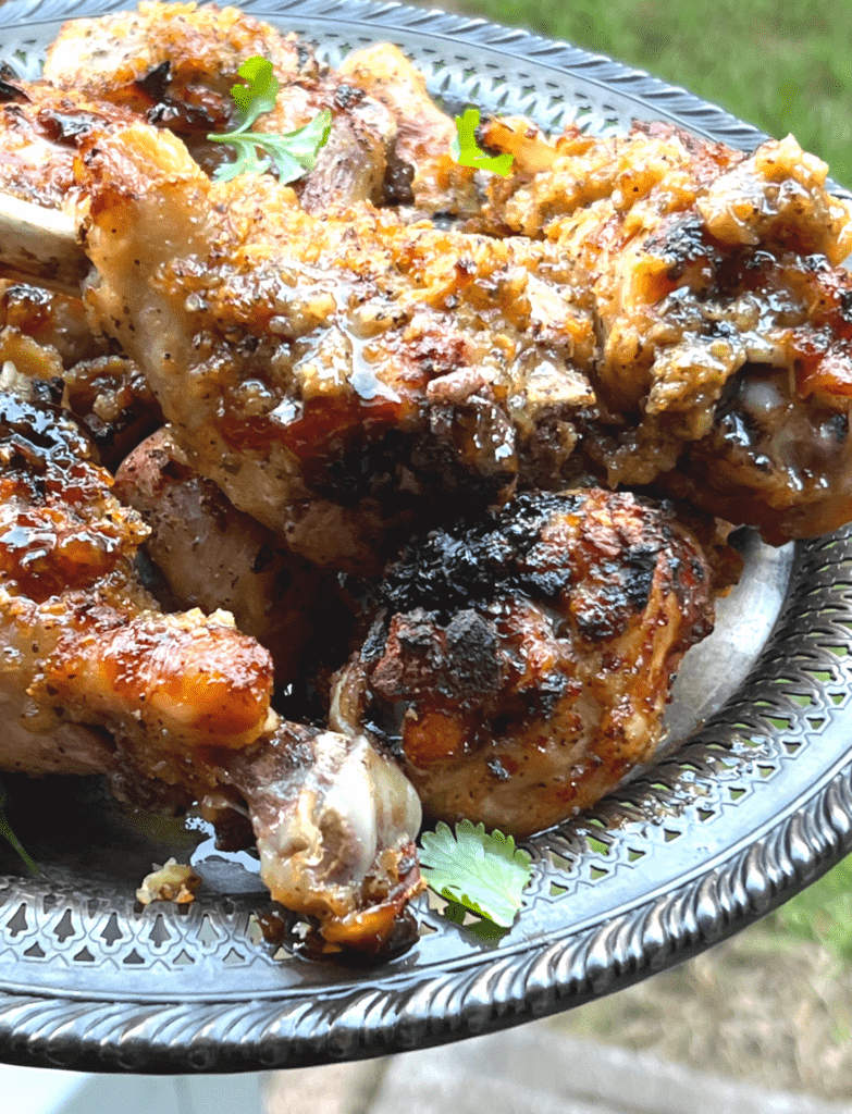 a pile of paleo huli huli chicken drumsticks on a silver platter with cilantro leaves on top