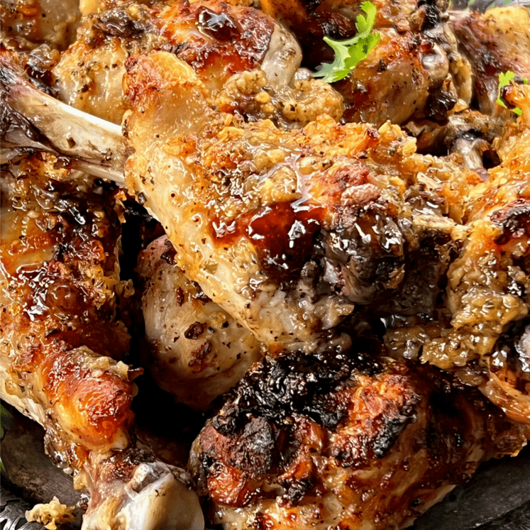 a pile of paleo huli huli chicken drumsticks on a silver platter with cilantro leaves on top