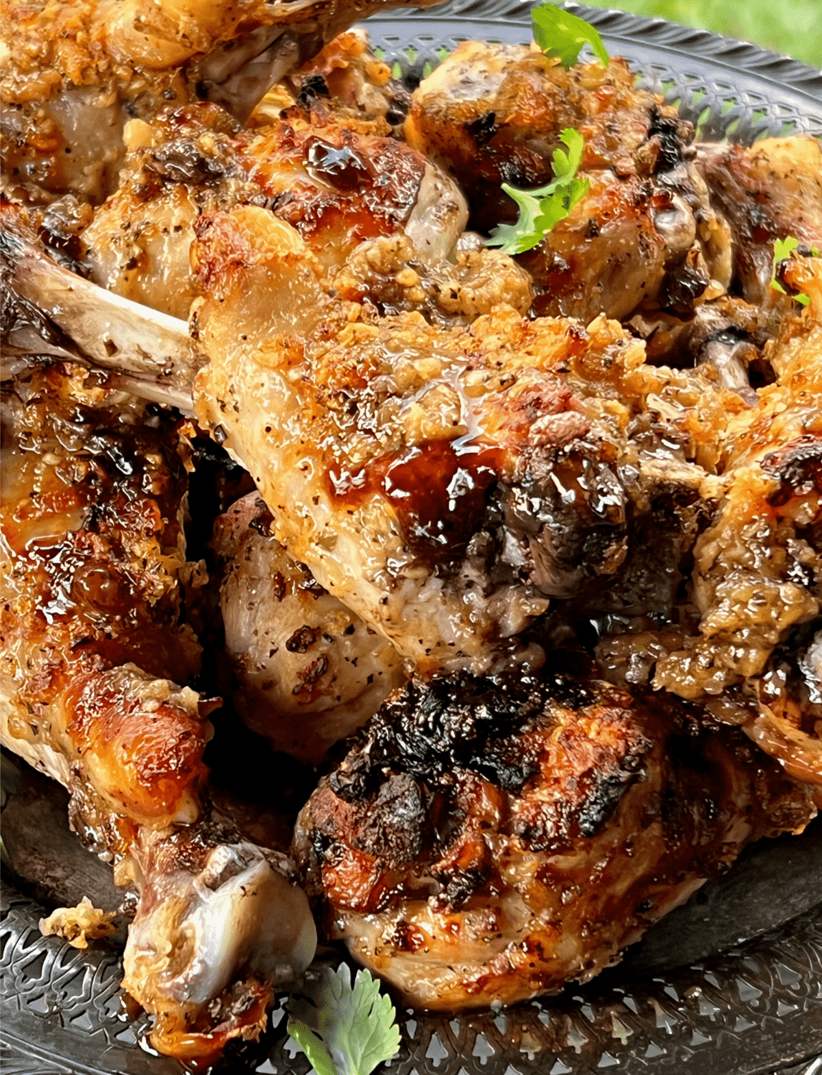 a pile of paleo huli huli chicken drumsticks on a silver platter with cilantro leaves on top