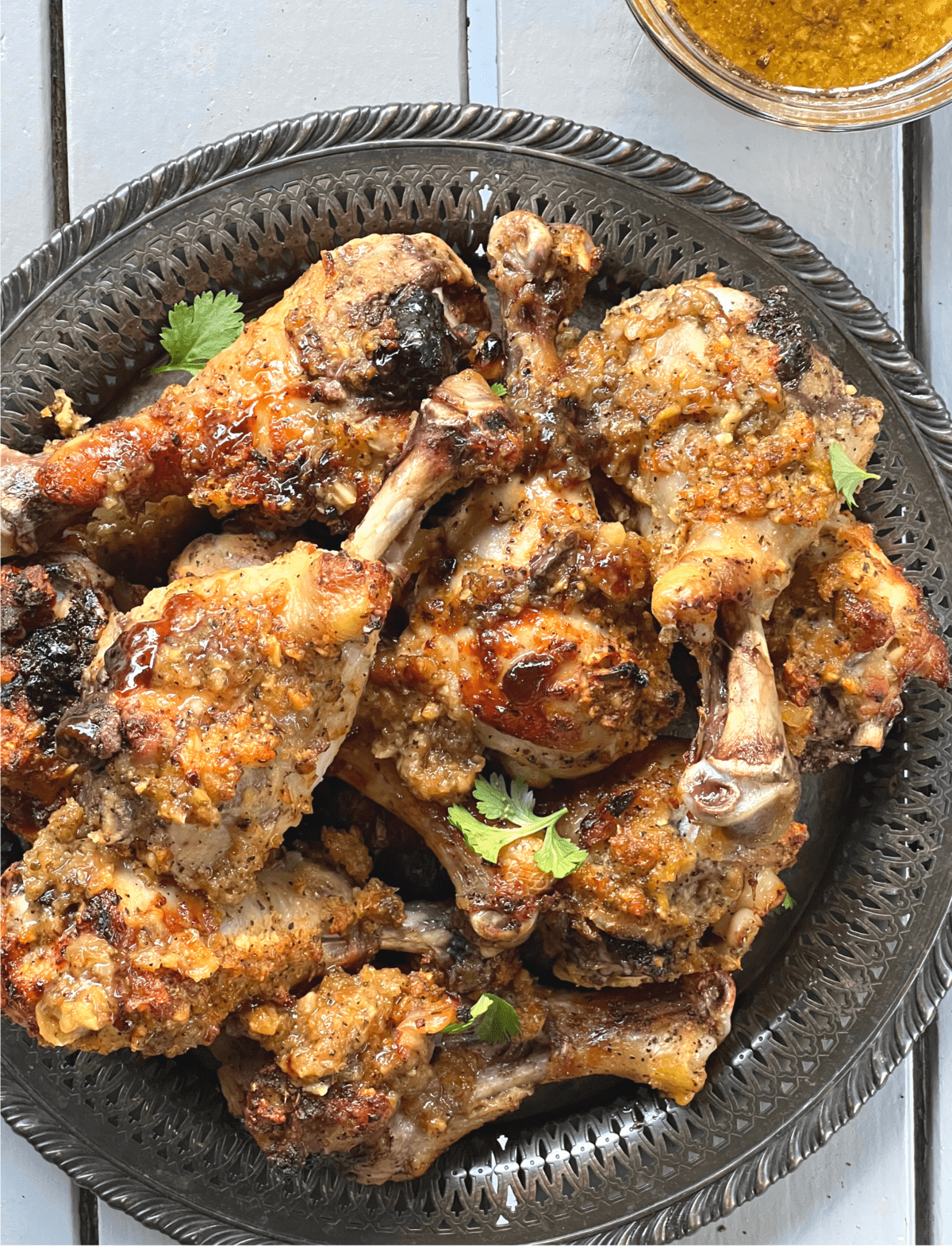 a pile of paleo huli huli chicken drumsticks on a silver platter with cilantro leaves on top