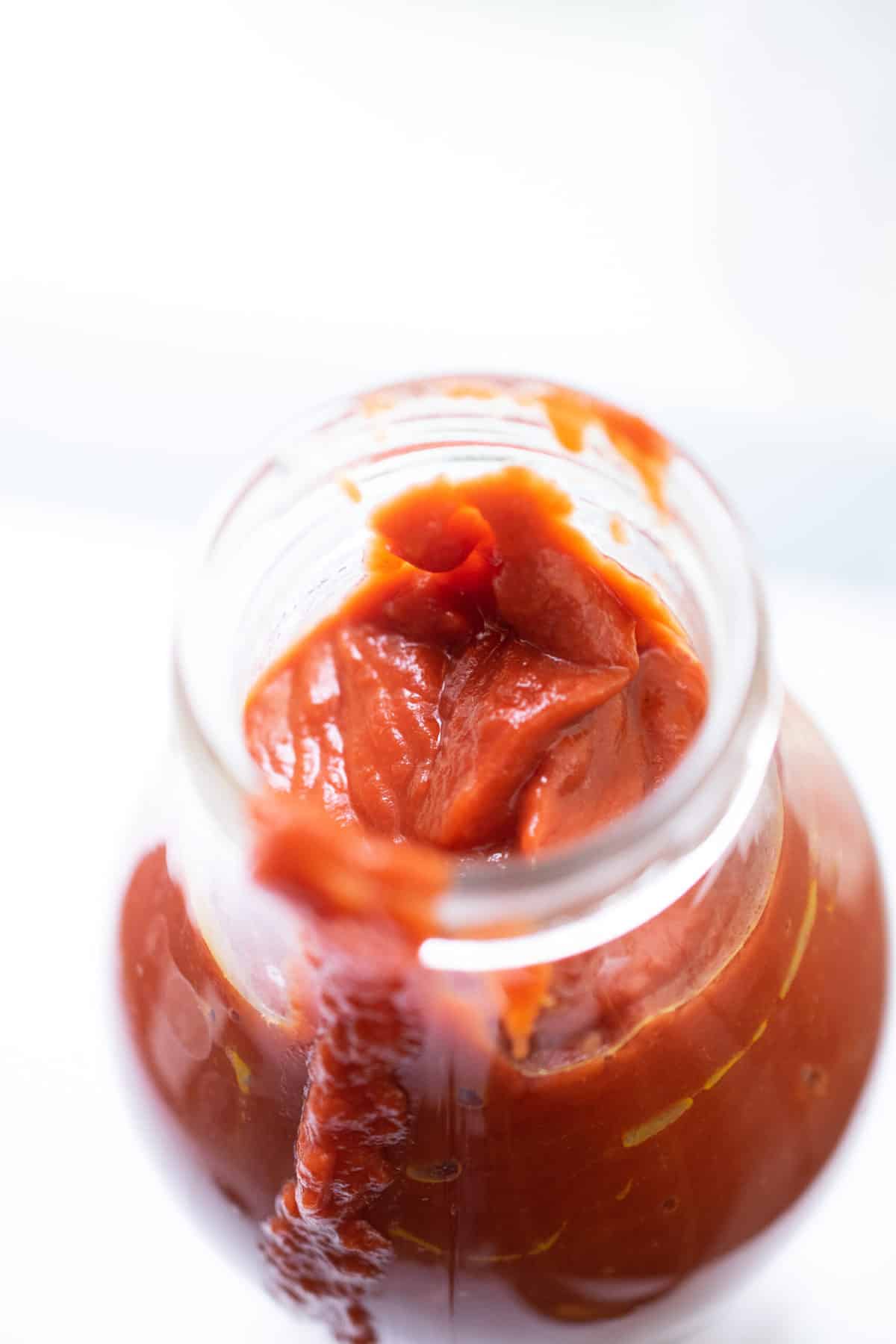 close up of a glass bottle mouth filled with thick red nomato sauce