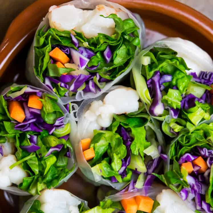 paleo spring rolls cut in half with shrimp and colorful veggies in a shallow brown bowl