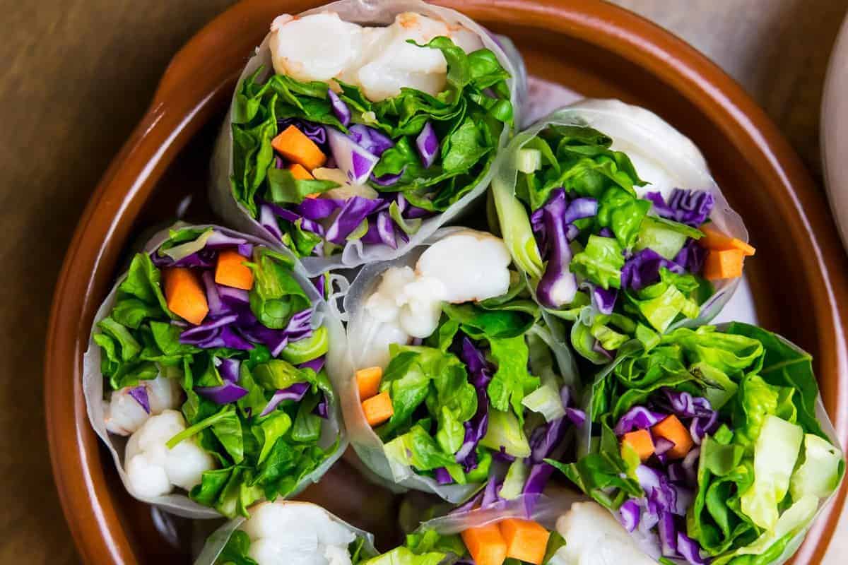 paleo spring rolls cut in half with shrimp and colorful veggies in a shallow brown bowl