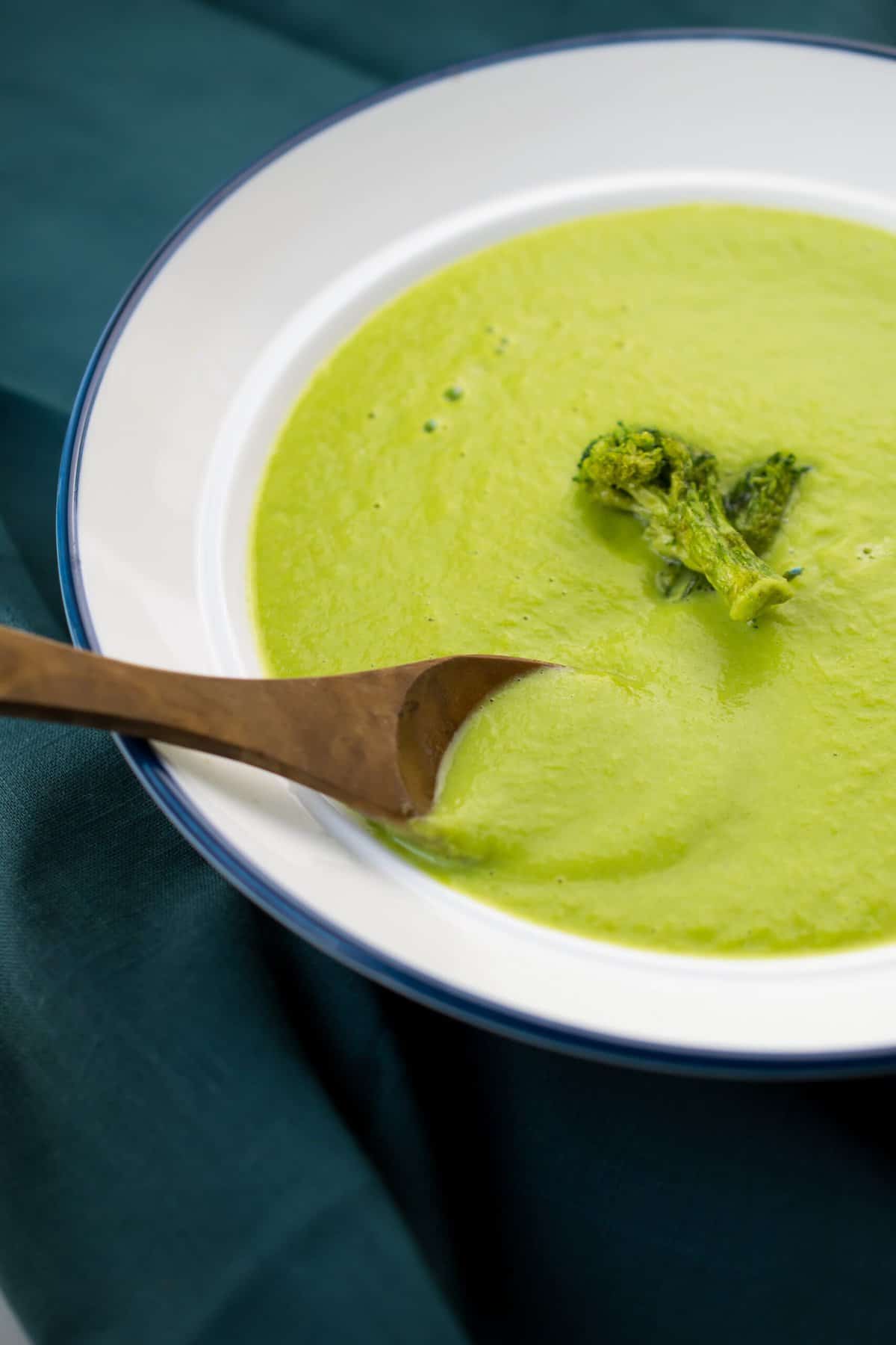 a wooden spoon scooping creamy whole30 asparagus soup from a white bowl, it's bright green and creamy