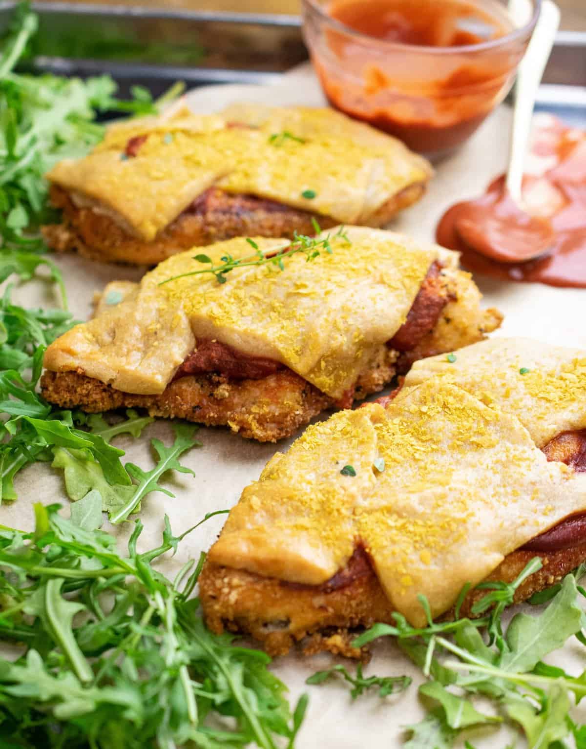 three gluten free breaded chicken cutlets topped with marinara and dairy free cheese on tray