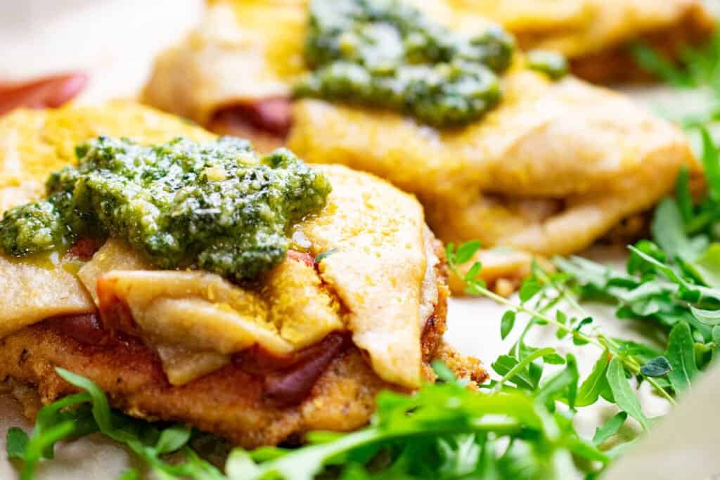 close up of paleo chicken parmesan topped with pesto on a bed of arugula 