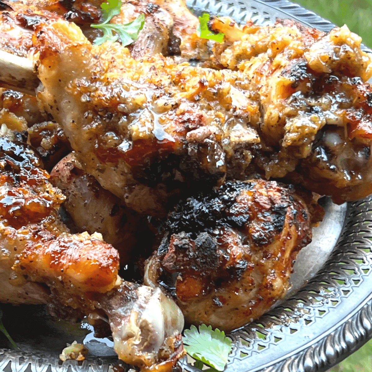 a pile of paleo huli huli chicken drumsticks on a silver platter with cilantro leaves on top