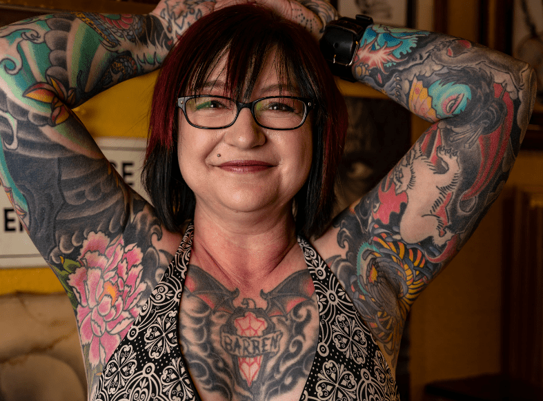 woman covered in tattoos with arms up and smiling