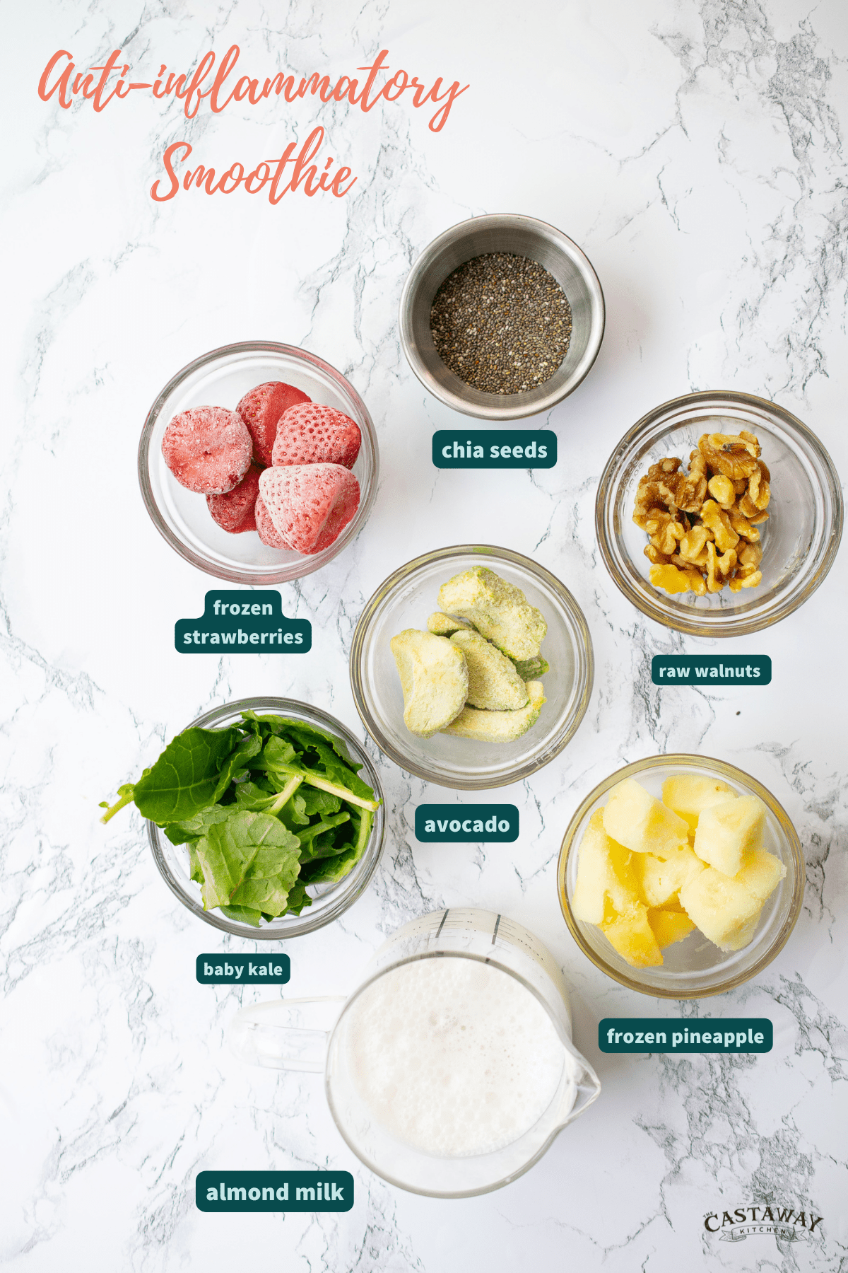 ingredients for anti-inflammatory smoothie in glass bowls on marble counter top; frozen strawberries, raw walnuts, avocado, baby kale, frozen pineapple, almond milk