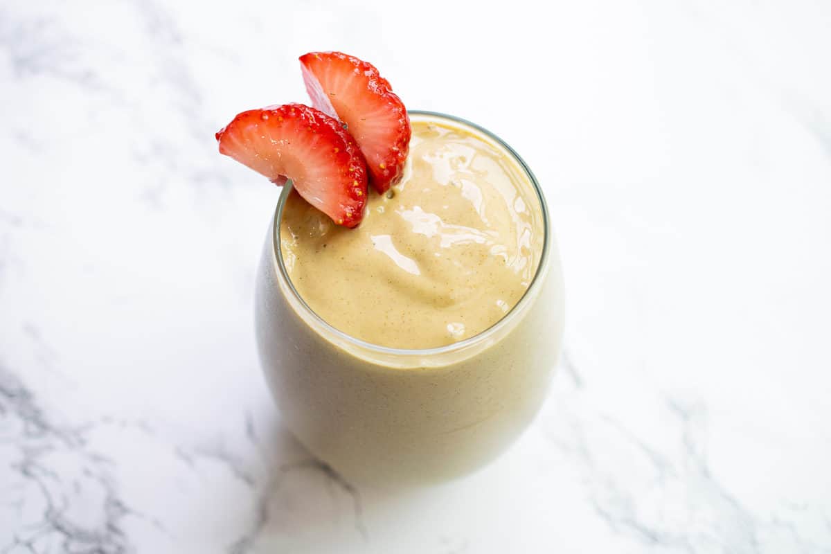 anti-inflammatory smoothie shot from above on white and grey marble countertop- glass has two slices of strawberry wedged on the rim