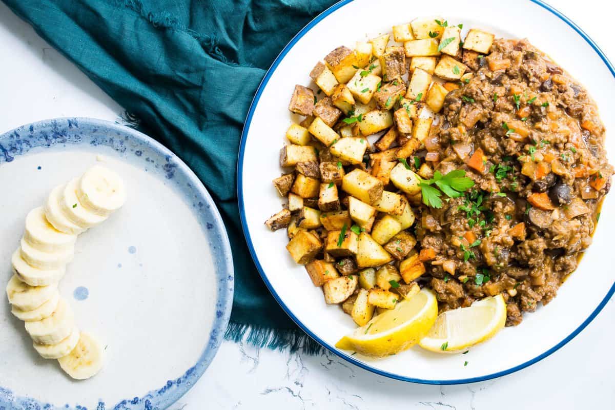 a plate of cuban picadilo on marble with crispy potatoes and a banana