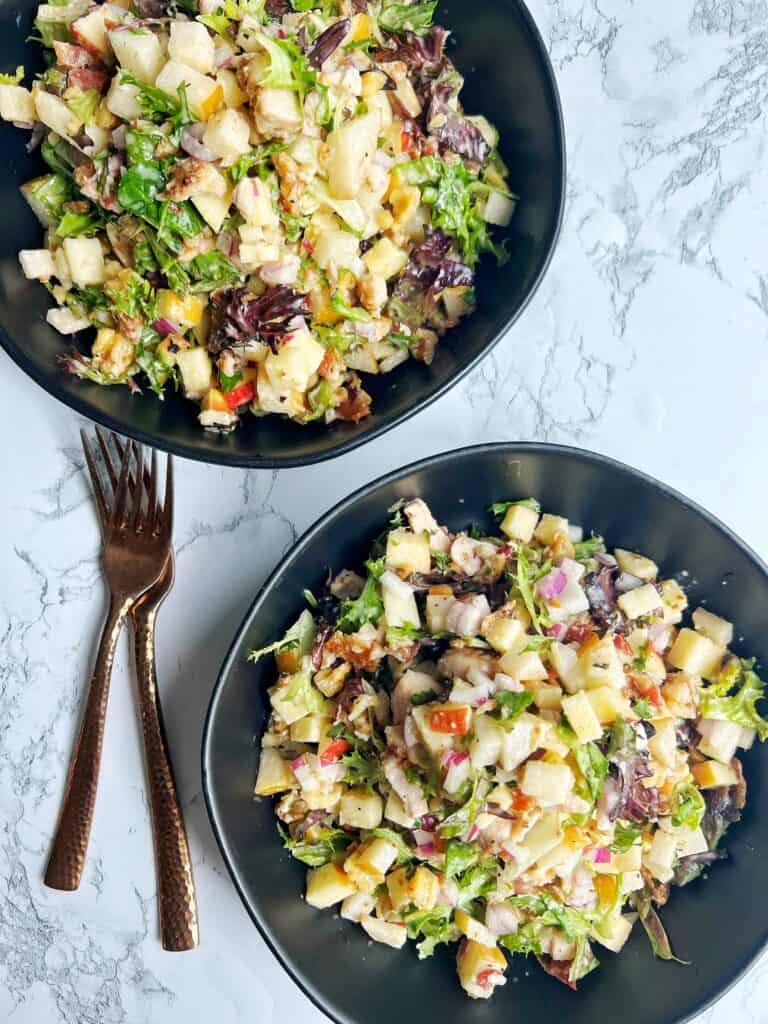 two black bowls on marble counter filled with chopped chicken and apple salad