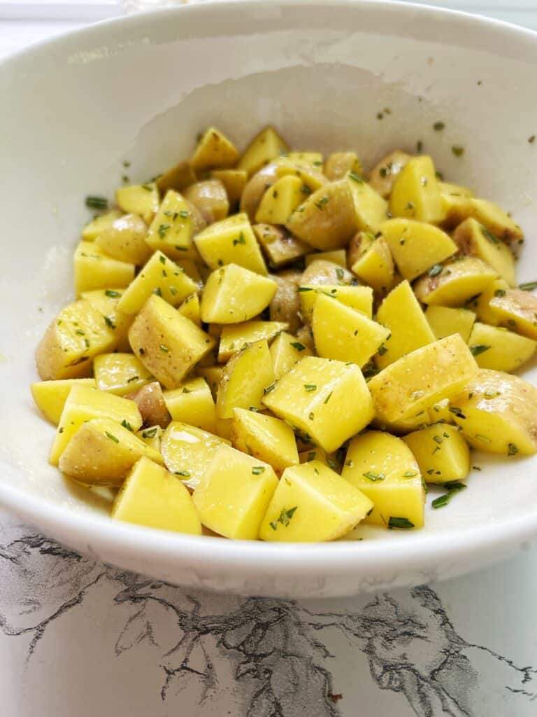 white bowl full of yukon gold potatoes with rosemary and salt 