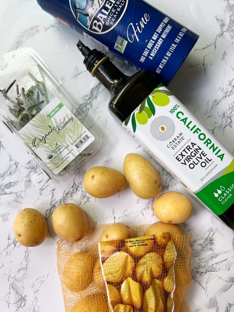 ingredients for air fryer potatoes: yukin gold, olive oil, salt, rosemary. On a counter