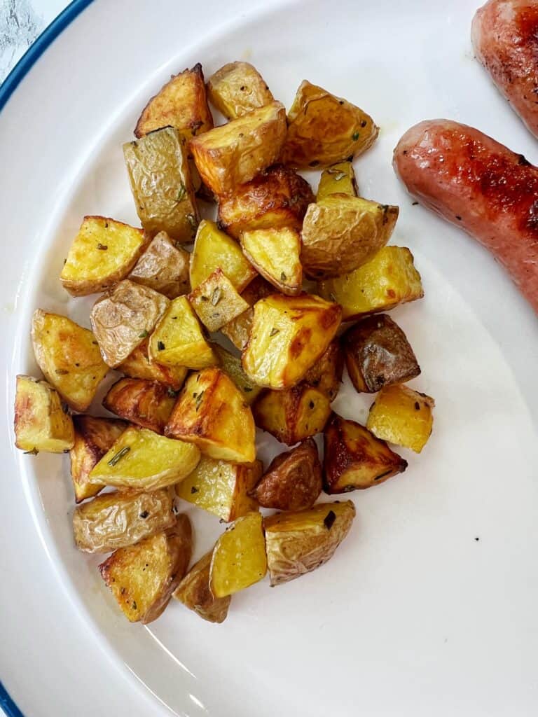 a white plate with crispy air fryer potatoes and sausage