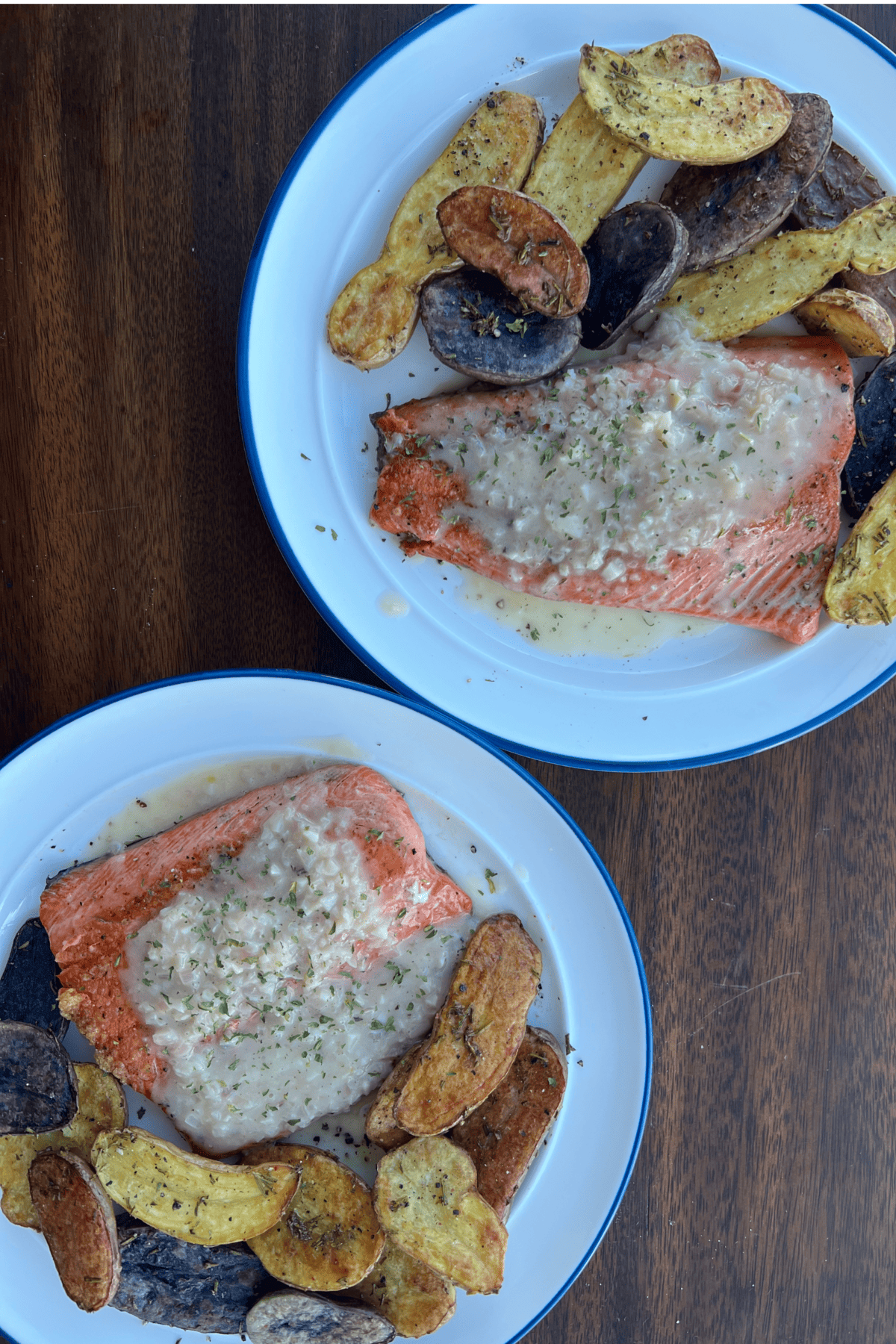 two white plates on a wooden table with pan seared salmon topped with buerre blanc with rosemary roasted fingerling potatoes