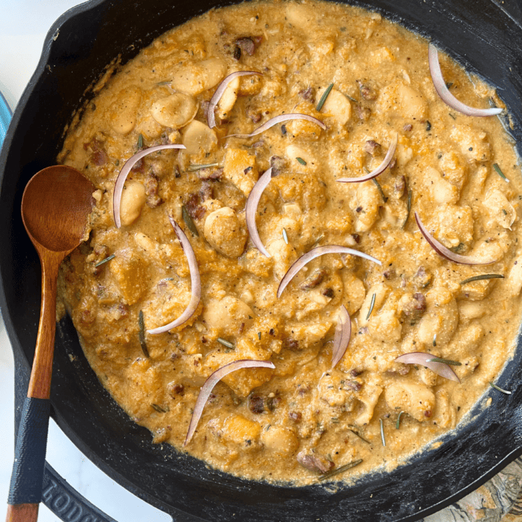 creamy pumpkin butter beans in a castiron skillet with a wooden spoon